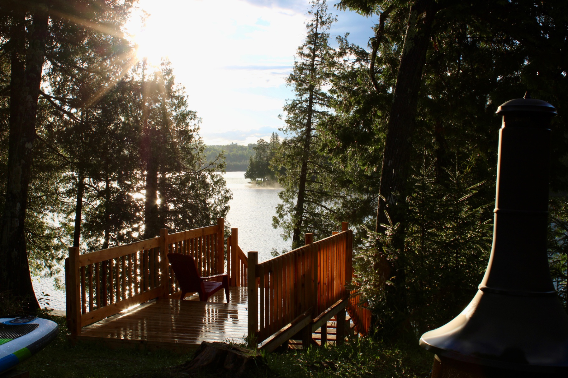 Sunlit lakeside deck with Muskoka chair overlooking the water at golden hour